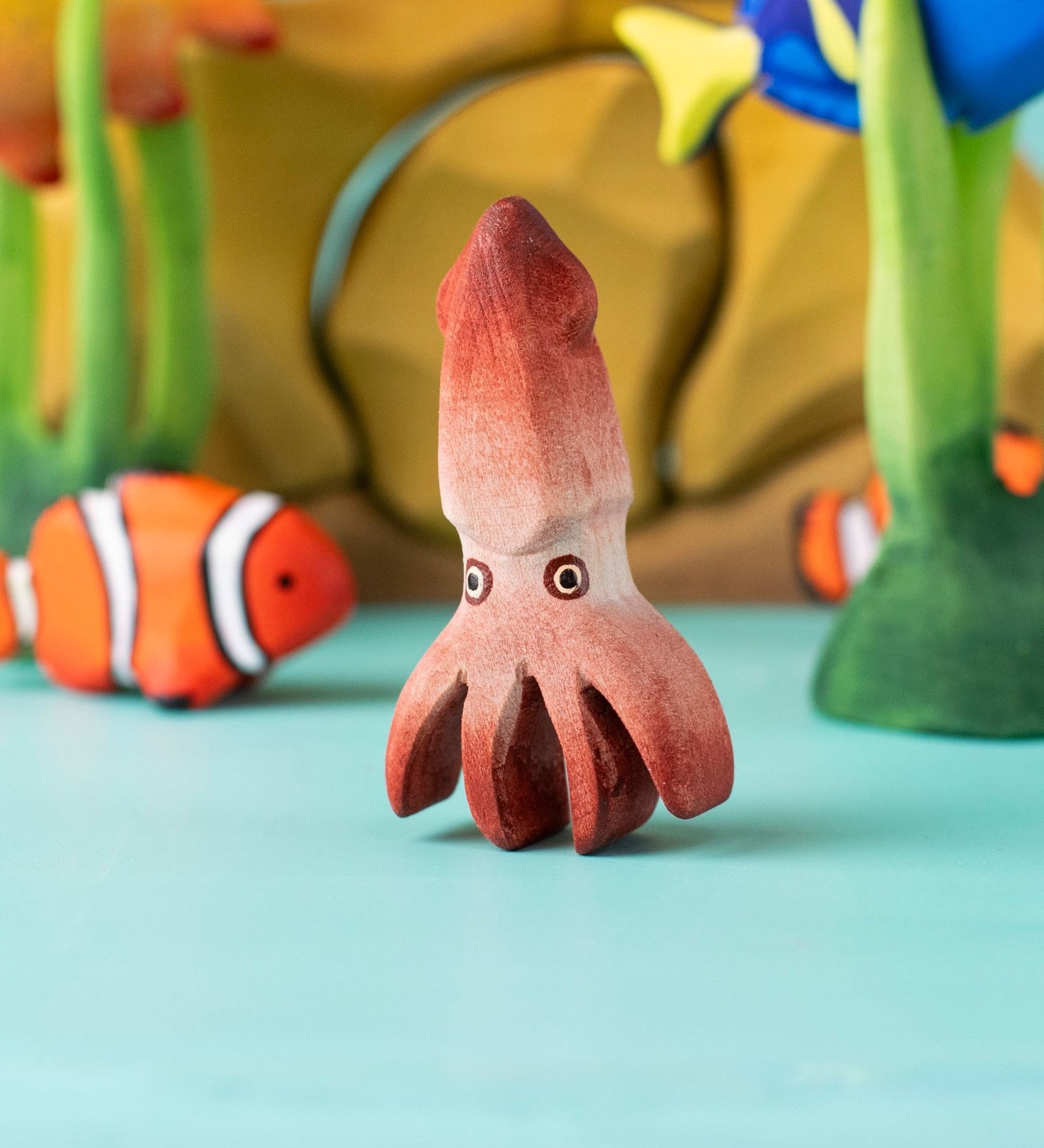 Bumbu handmade and hand painted wooden squid figure with cute painted on eyes with other Bumbu ocean themed figures in the background 