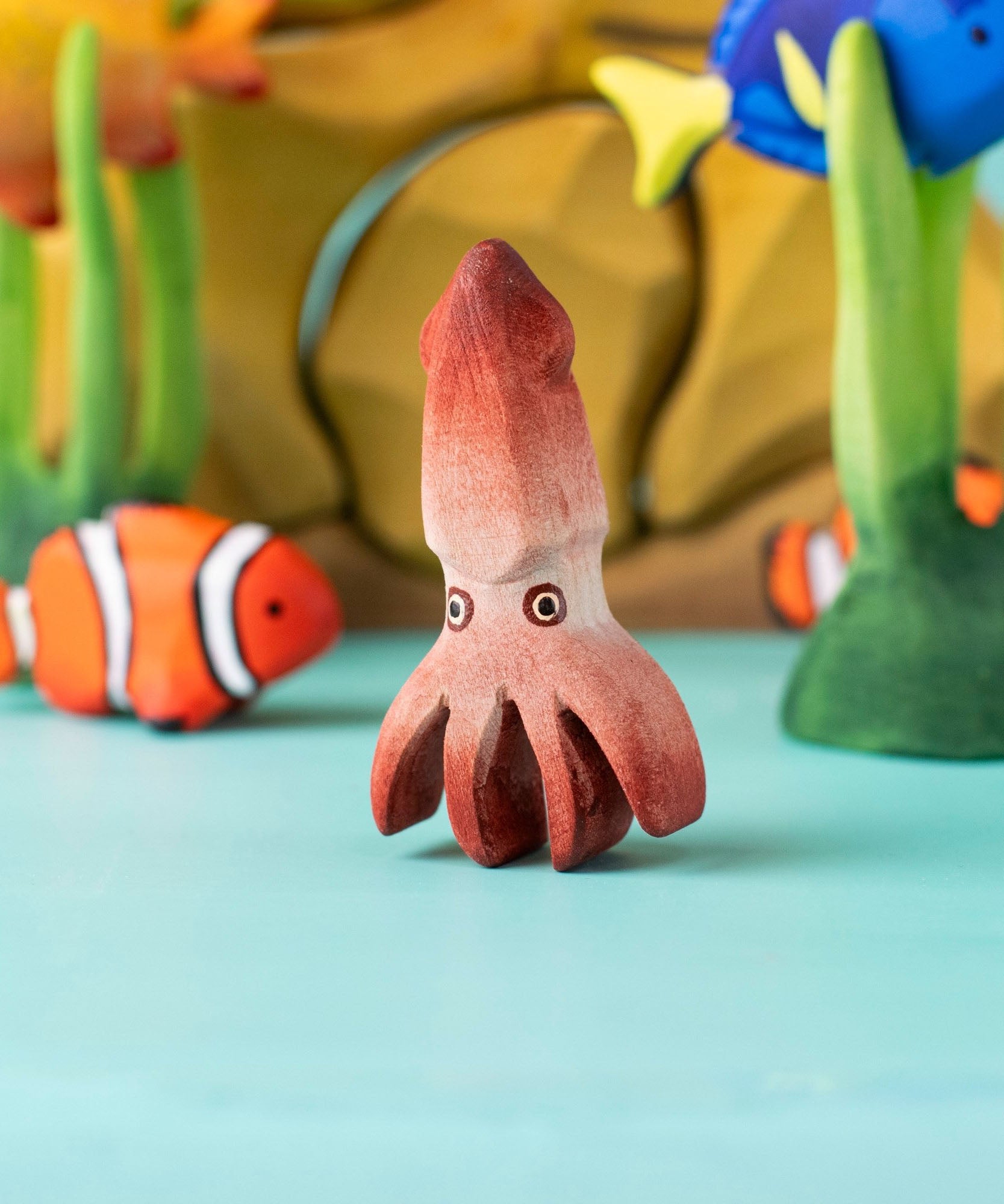Bumbu handmade and hand painted wooden squid figure with cute painted on eyes with other Bumbu ocean themed figures in the background 