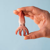 An adult hand holding the Bumbu handmade and hand painted wooden squid figure showing scale