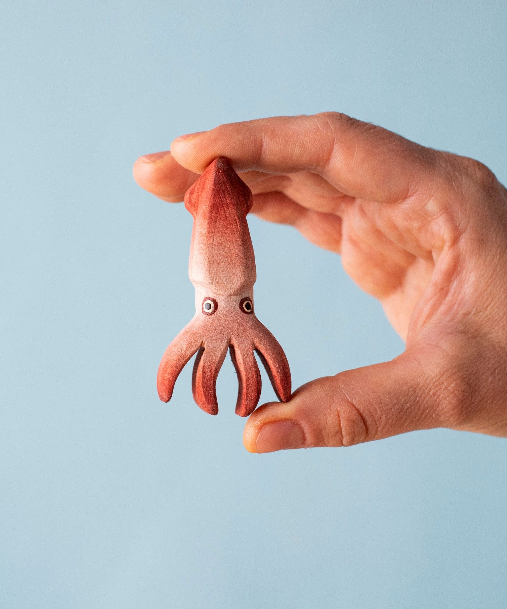 An adult hand holding the Bumbu handmade and hand painted wooden squid figure showing scale