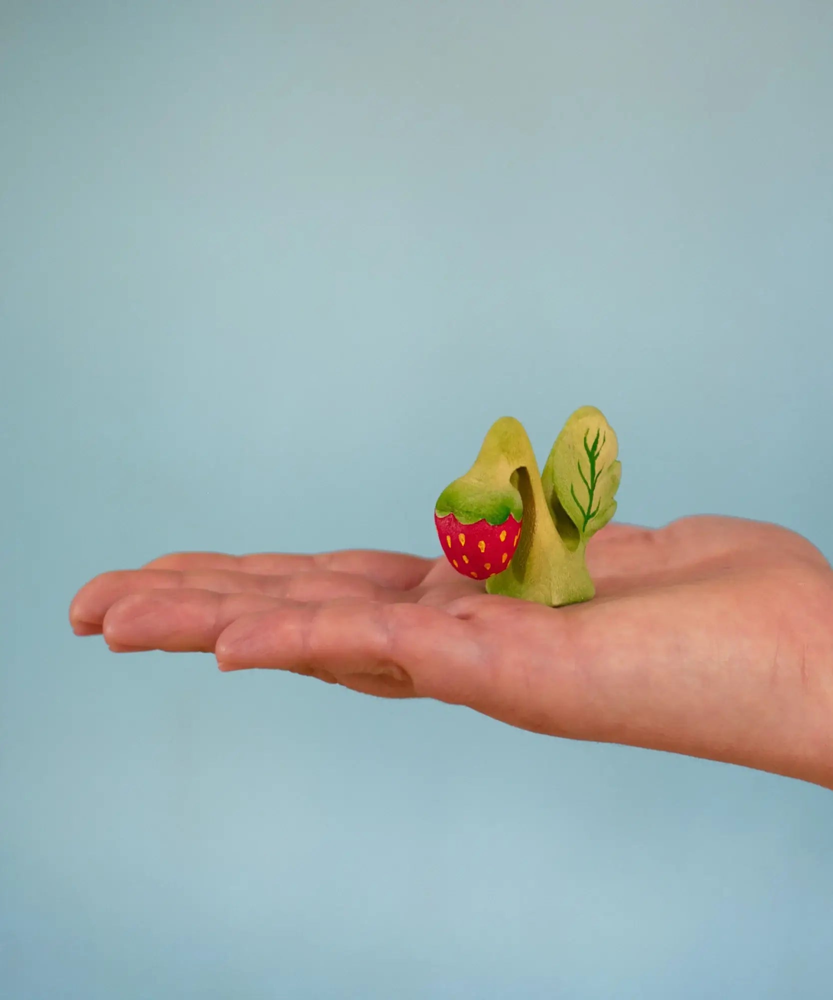 Bumbu handcrafted wooden strawberry plant standing on a adult hand