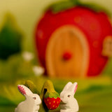 Bumbu handcrafted wooden strawberry plant figure standing next to white rabbit and a strawberry house in the background
