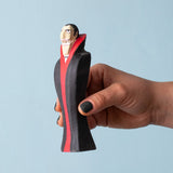 An adult hand holding the Bumbu handmade and hand painted dracula the vampire figure showing its size
