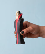 An adult hand holding the Bumbu handmade and hand painted dracula the vampire figure showing its size