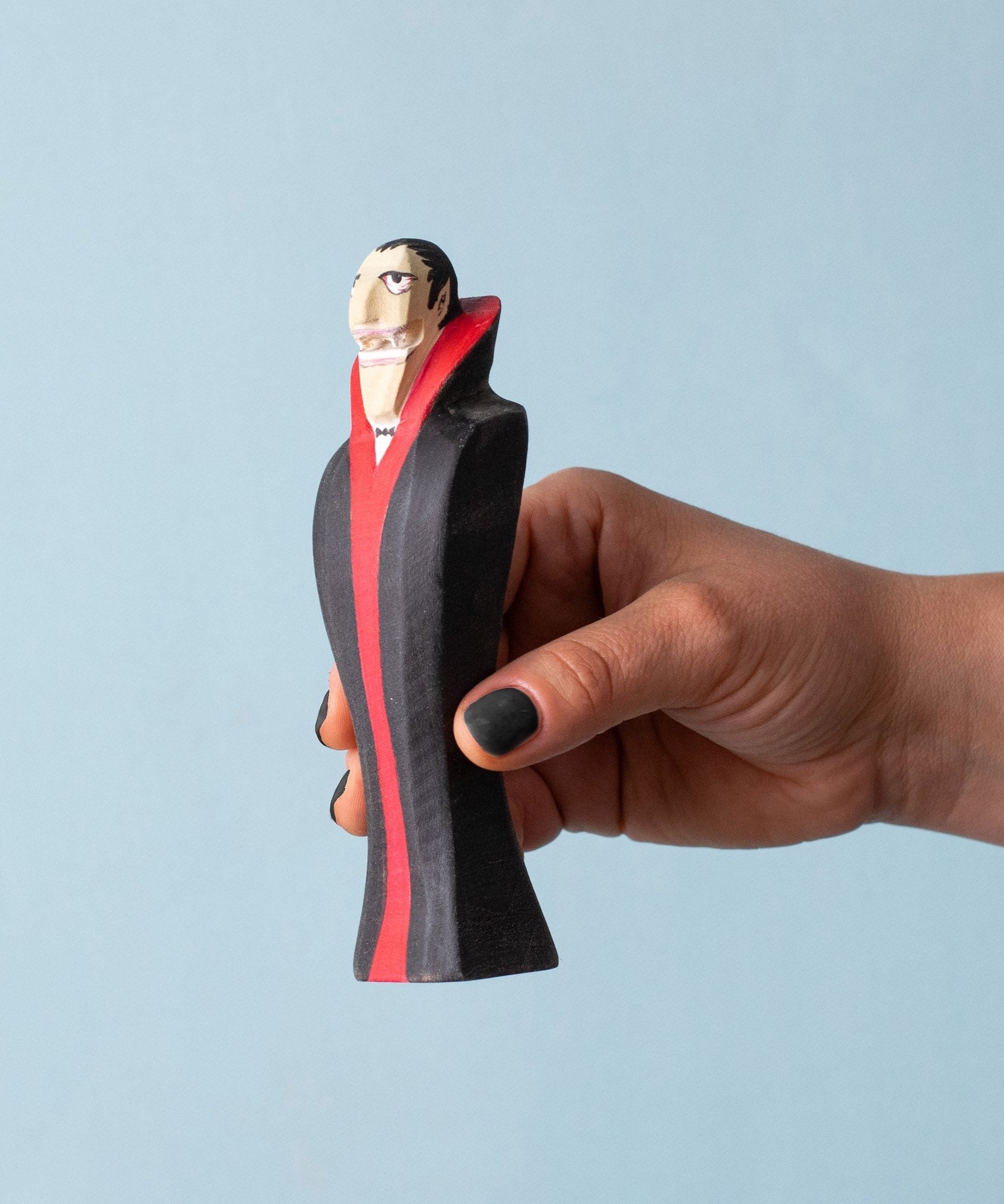 An adult hand holding the Bumbu handmade and hand painted dracula the vampire figure showing its size