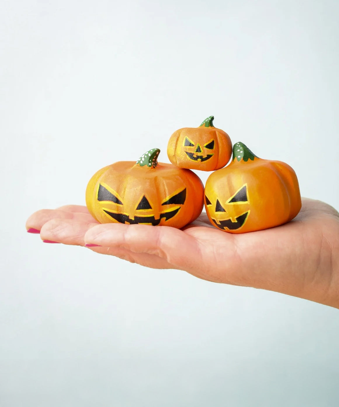 The small, medium and large Bumbu Toys Halloween Pumpkins are being held in a persons palm in a stacked formation