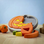 The Bumbu Toys Halloween Pumpkin Puzzle with a grey puzzle board, is an orange and yellow pumpkin puzzle, with removable pumpkin sections. Perfect for Halloween games. This image shows part of the pumpkin puzzle in the wooden board, and some pieces in front of the puzzle.