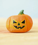 The small Bumbu Toys Halloween Pumpkin is hand made and hand painted in orange, with yellow and black facial features and a green and white spotted stem. This image gives a lose up of the pumpkin grooves, giving it a realistic look