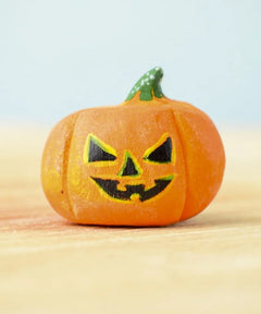 The small Bumbu Toys Halloween Pumpkin is hand made and hand painted in orange, with yellow and black facial features and a green and white spotted stem. This image gives a lose up of the pumpkin grooves, giving it a realistic look