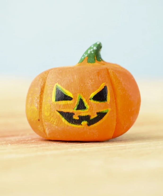 The small Bumbu Toys Halloween Pumpkin is hand made and hand painted in orange, with yellow and black facial features and a green and white spotted stem. This image gives a lose up of the pumpkin grooves, giving it a realistic look