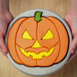 A person holding the Bumbu Toys Halloween Pumpkin Puzzle - Grey, in their hands. The image is a close up view of the pumpkin puzzle from above, showing the different puzzle sections
