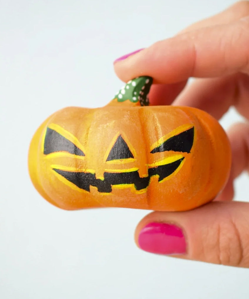 The Bumbu Toys Halloween Pumpkin - Large is being held in between a persons fingers, they are wearing pink nail varnish. In this image you can really see the pumpkin texture and paintwork