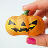 The Bumbu Toys Halloween Pumpkin - Large is being held in between a persons fingers, they are wearing pink nail varnish. In this image you can really see the pumpkin texture and paintwork