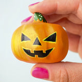 The medium Bumbu Toys Halloween Pumpkin is being held in between a persons fingers and they are wearing pink nail varnish. In this image, you can really see the grooves of the pumpkin, giving it a realistic texture