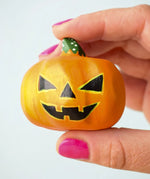 The medium Bumbu Toys Halloween Pumpkin is being held in between a persons fingers and they are wearing pink nail varnish. In this image, you can really see the grooves of the pumpkin, giving it a realistic texture