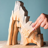 Set of five Bumbu toys wooden mountain cliff pieces, each uniquely carved and painted to look like rugged rock formations. Designed for open-ended and small-world play. Available from Babipur.