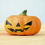 Bumbu Toys Halloween Pumpkin - Large. A spooky addition to any Halloween party, this large wooden pumpkin is orange, with a yellow and black face and a green and white spotted stem on top. The pumpkin sits on a wooden table and light blue background