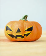Bumbu Toys Halloween Pumpkin - Large. A spooky addition to any Halloween party, this large wooden pumpkin is orange, with a yellow and black face and a green and white spotted stem on top. The pumpkin sits on a wooden table and light blue background