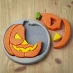 The Bumbu Toys Halloween Pumpkin Puzzle - Grey is laid on a wooden table. Part of the puzzle is in the grey puzzle board, with smaller pieces placed next to the puzzle
