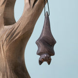 Bumbu Toys handmade and hand painted wooden bat figure available at Babipur with its wings wrapped up. Features a small hole with a thread looping through for the bat to hang off a tree