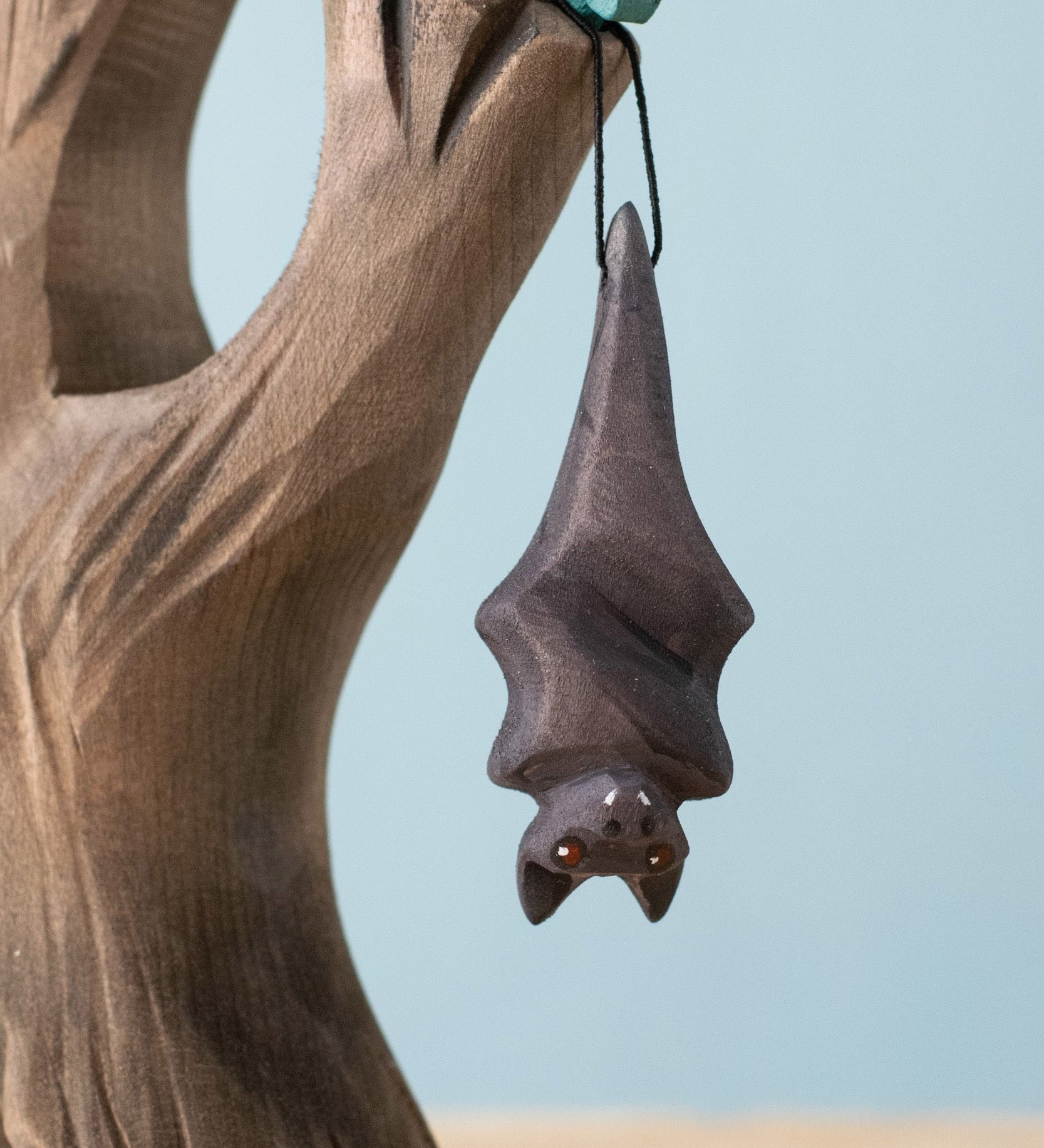 Bumbu Toys handmade and hand painted wooden bat figure available at Babipur with its wings wrapped up. Features a small hole with a thread looping through for the bat to hang off a tree