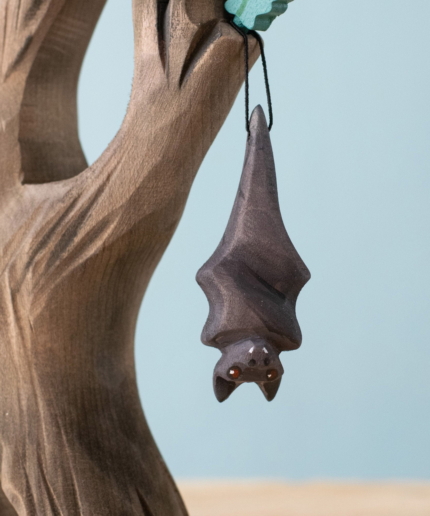 Bumbu Toys handmade and hand painted wooden bat figure available at Babipur with its wings wrapped up. Features a small hole with a thread looping through for the bat to hang off a tree