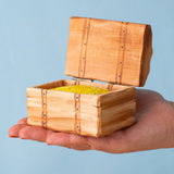 An adult hand holding the Bumbu handmade and hand painted wooden treasure chest available at Babipur showing size