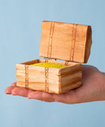 An adult hand holding the Bumbu handmade and hand painted wooden treasure chest available at Babipur showing size