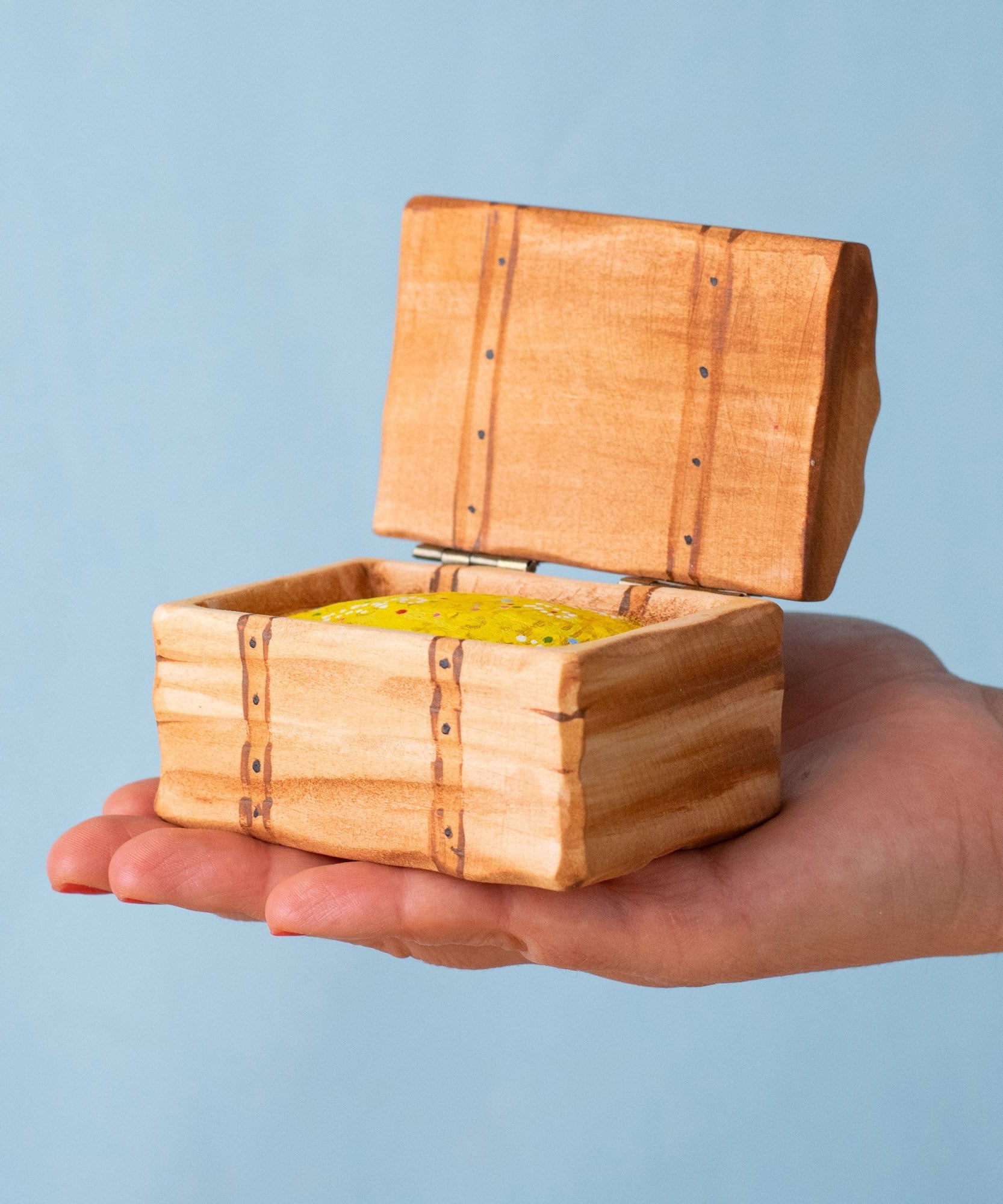 An adult hand holding the Bumbu handmade and hand painted wooden treasure chest available at Babipur showing size