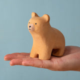 An adult hand holding the Bumbu handmade and hand painted wooden brown curious bear figure showing