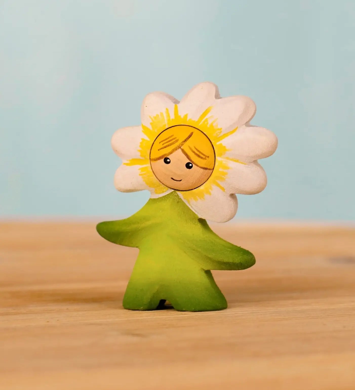 Bumbu handcrafted wooden daisy flower child figure with hand painted facial features standing on a wooden surface