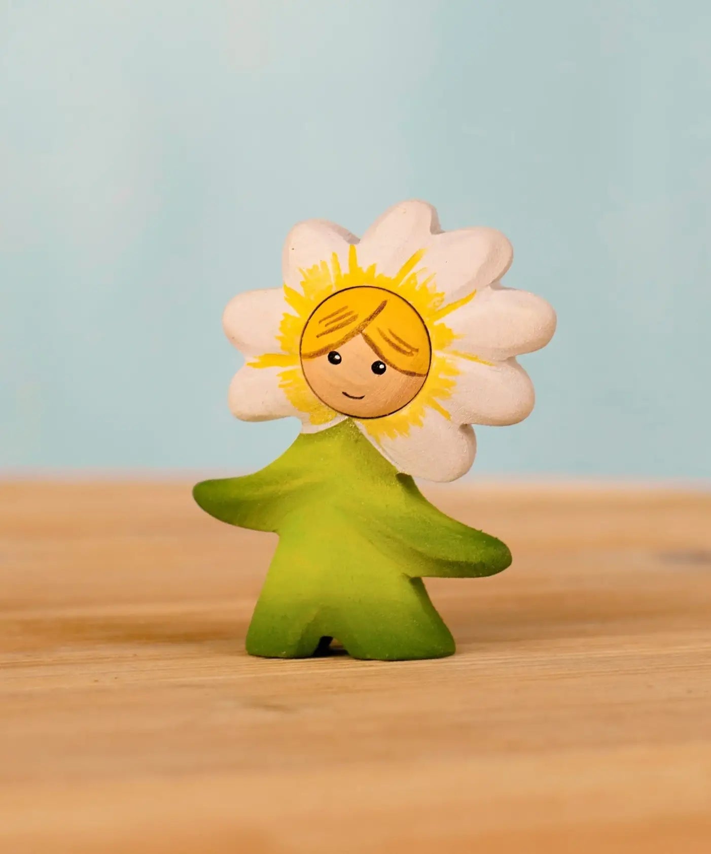 Bumbu handcrafted wooden daisy flower child figure with hand painted facial features standing on a wooden surface