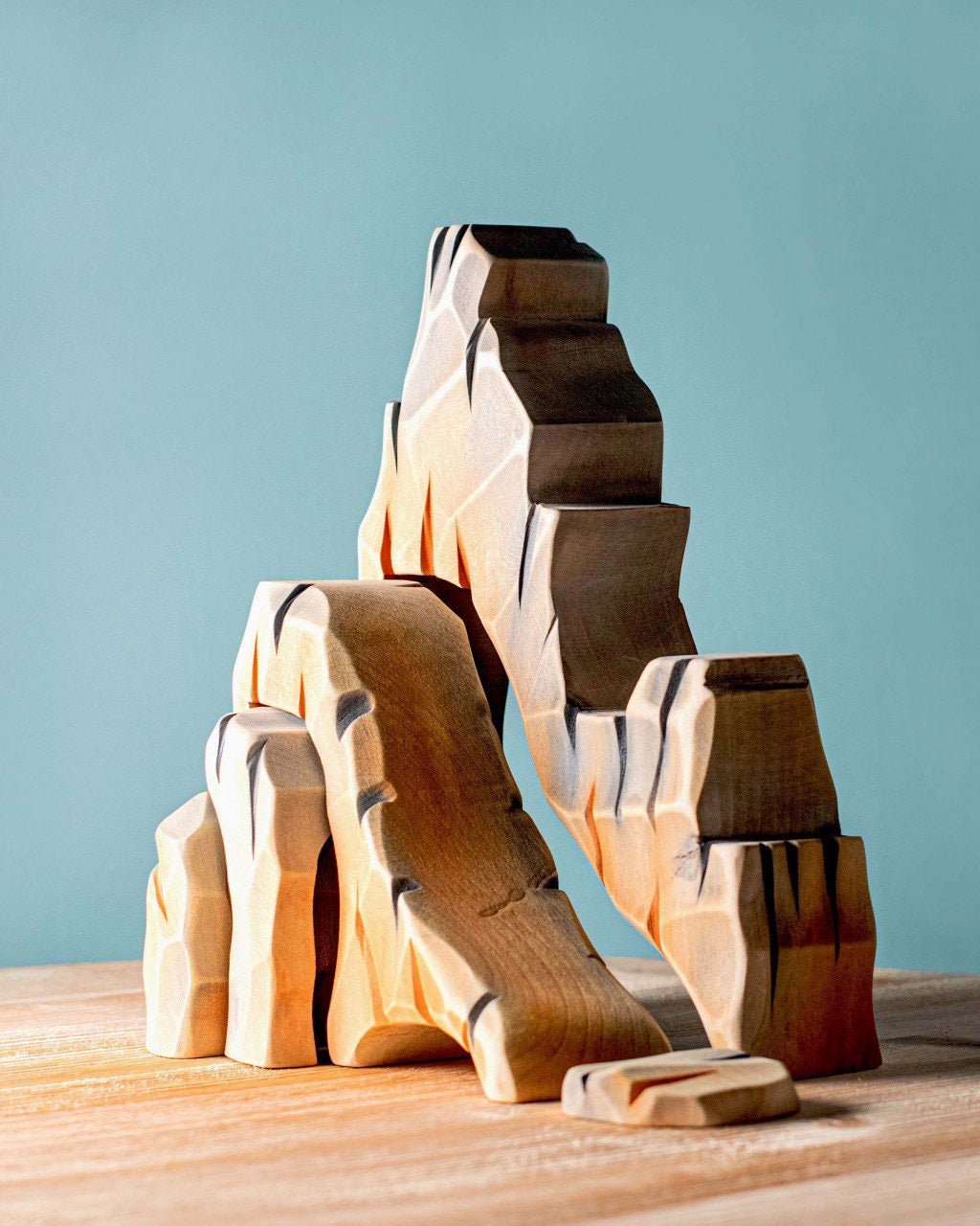 Bumbu Mountain Cliffs wooden toy set, featuring five handcrafted cliff pieces in natural earthy tones. The carved shapes stack and arrange to create a rocky mountain landscape for imaginative small-world play. Sold by Babipur.