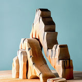 Bumbu Mountain Cliffs wooden toy set, featuring five handcrafted cliff pieces in natural earthy tones. The carved shapes stack and arrange to create a rocky mountain landscape for imaginative small-world play. Sold by Babipur.