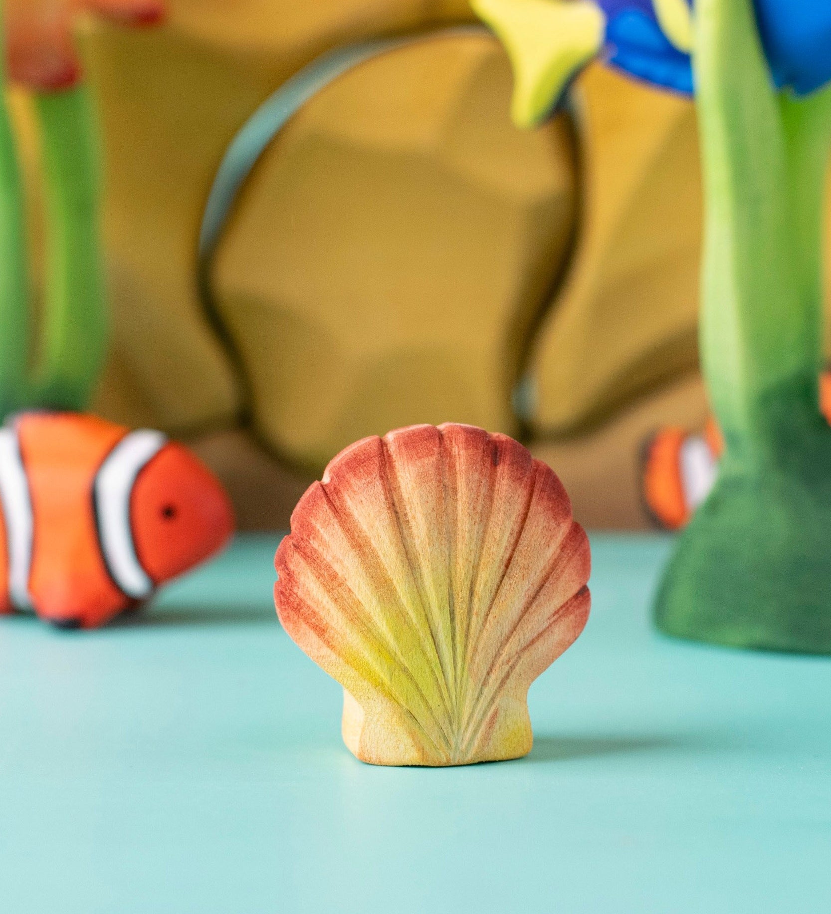 Bumbu handmade and hand painted orange and red wooden seashell figure  with a clownfish and reef set in the background