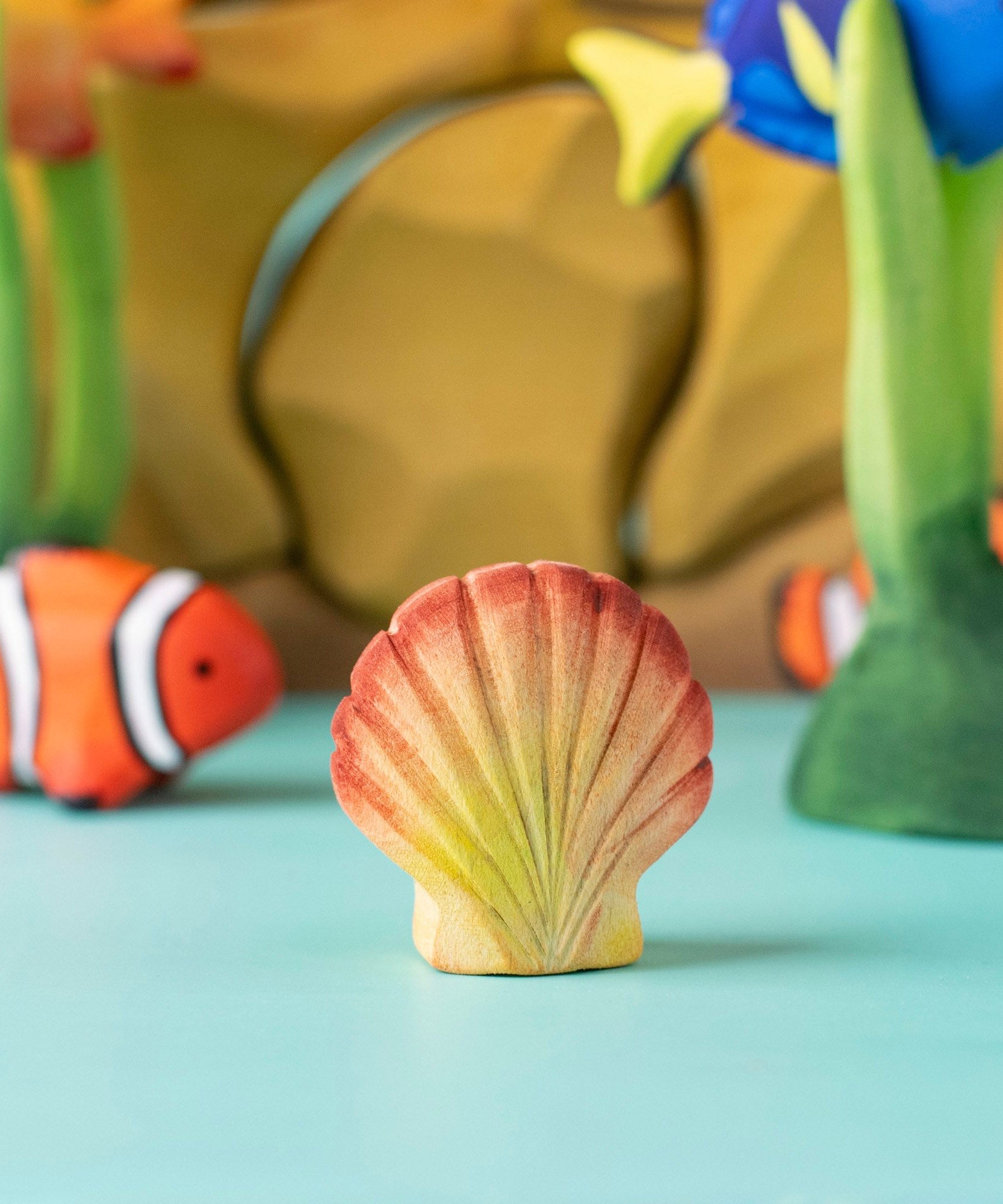 Bumbu handmade and hand painted orange and red wooden seashell figure  with a clownfish and reef set in the background