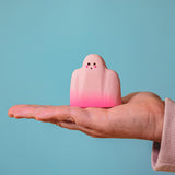 An adult hand holding the Bumbu handmade and hand painted wooden pink ghost figure for size reference