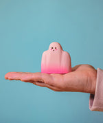 An adult hand holding the Bumbu handmade and hand painted wooden pink ghost figure for size reference