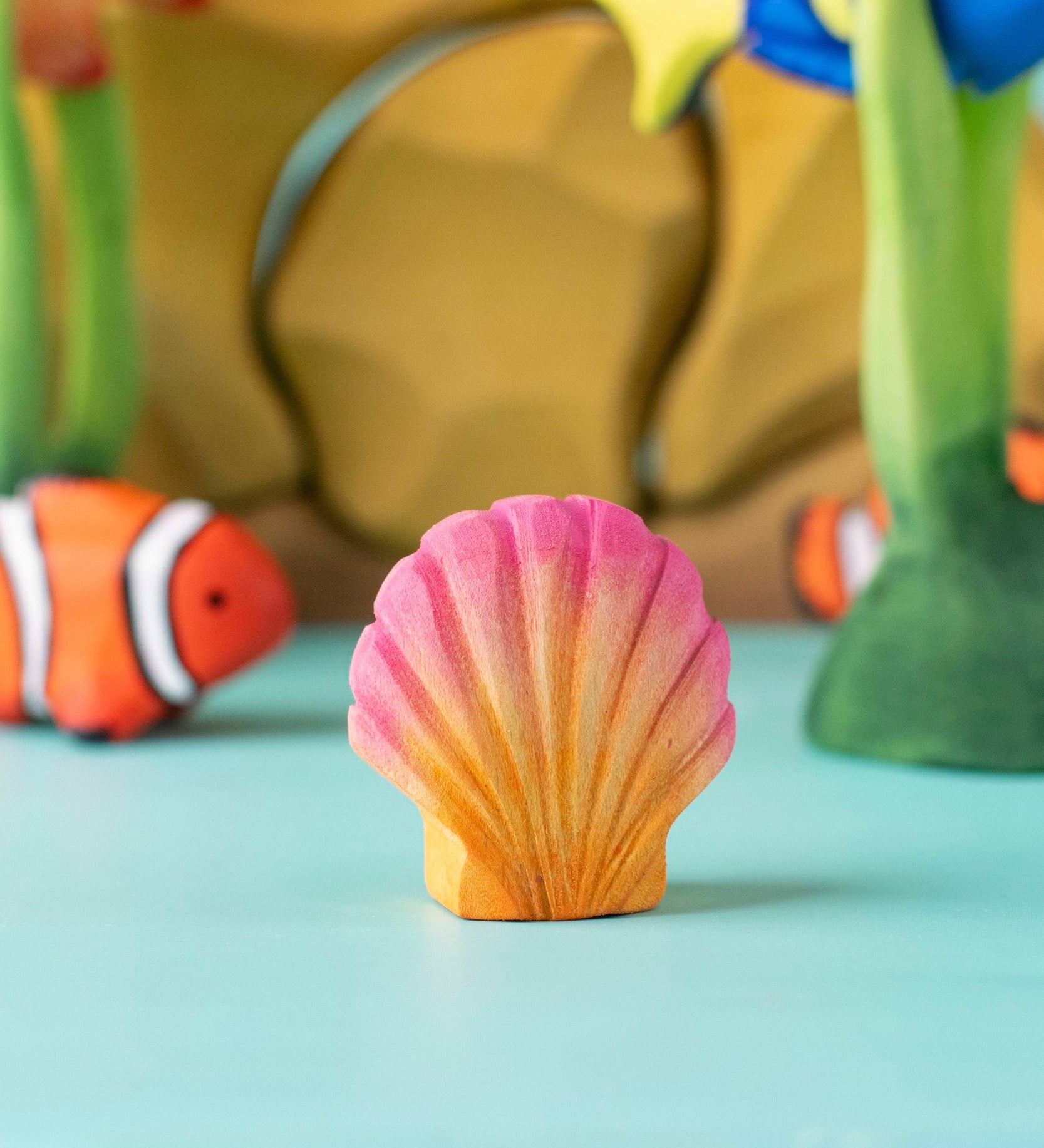 Bumbu handmade and hand painted orange and pink wooden seashell figure  with a clownfish and reef set in the background
