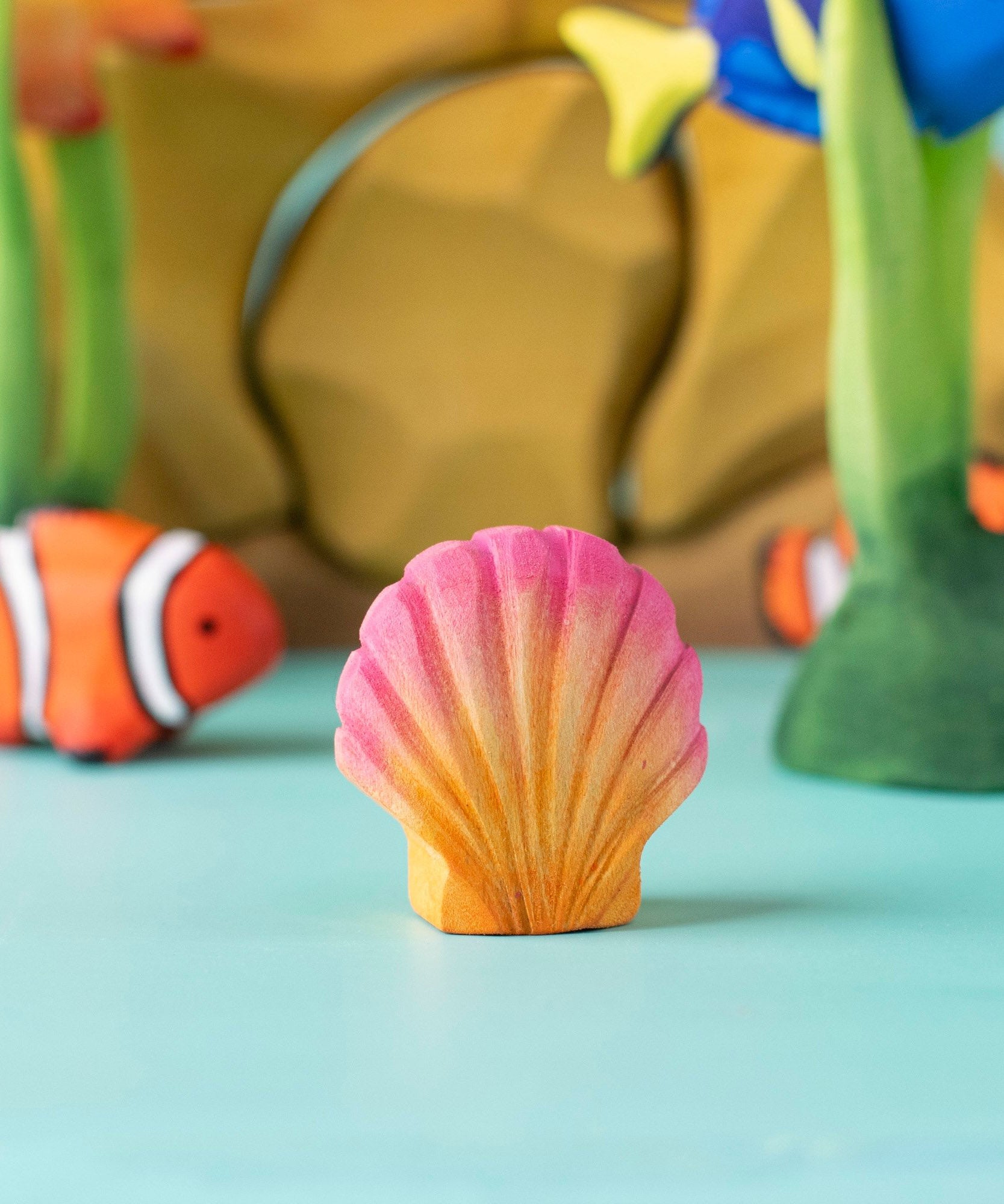 Bumbu handmade and hand painted orange and pink wooden seashell figure  with a clownfish and reef set in the background