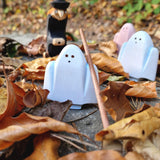 A group of white and pink Bumbu wooden ghost figures and a witch figure standing on autumn leaves