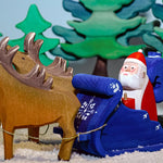 Santa is getting ready to deliver the toys on Christmas Eve! Santa is sat in the back of the Snow Sleigh with green wooden Bumbu trees in the background
