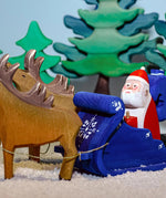 Santa is getting ready to deliver the toys on Christmas Eve! Santa is sat in the back of the Snow Sleigh with green wooden Bumbu trees in the background