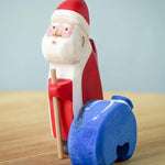 Santa has put down the blue sack with the image showing Santa holding onto a wooden stick with the blue wooden sack next to the figure