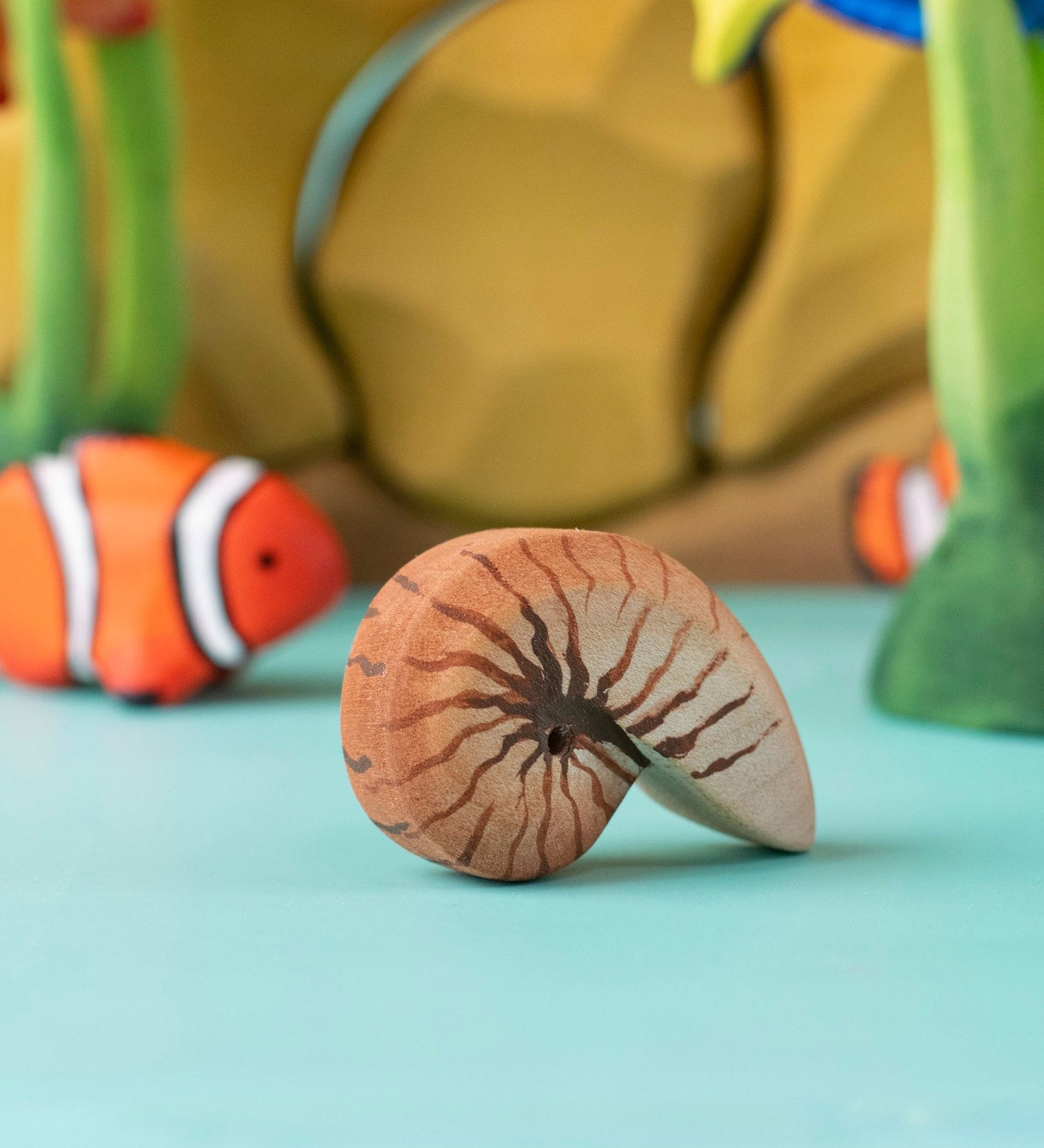 Bumbu handmade and hand painted brown wooden spiral shell figure with a clownfish and reef set in the background
