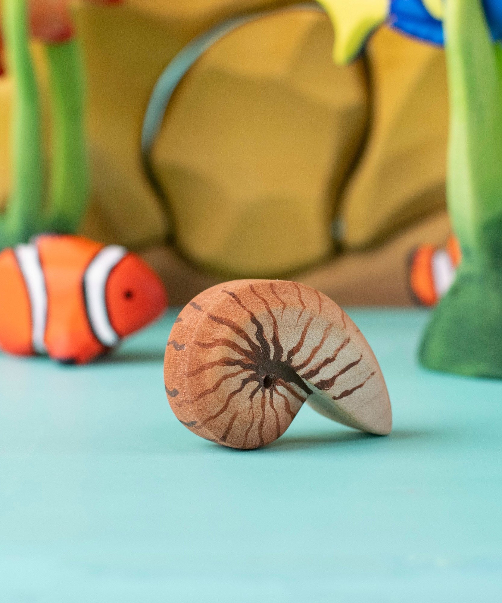 Bumbu handmade and hand painted brown wooden spiral shell figure with a clownfish and reef set in the background