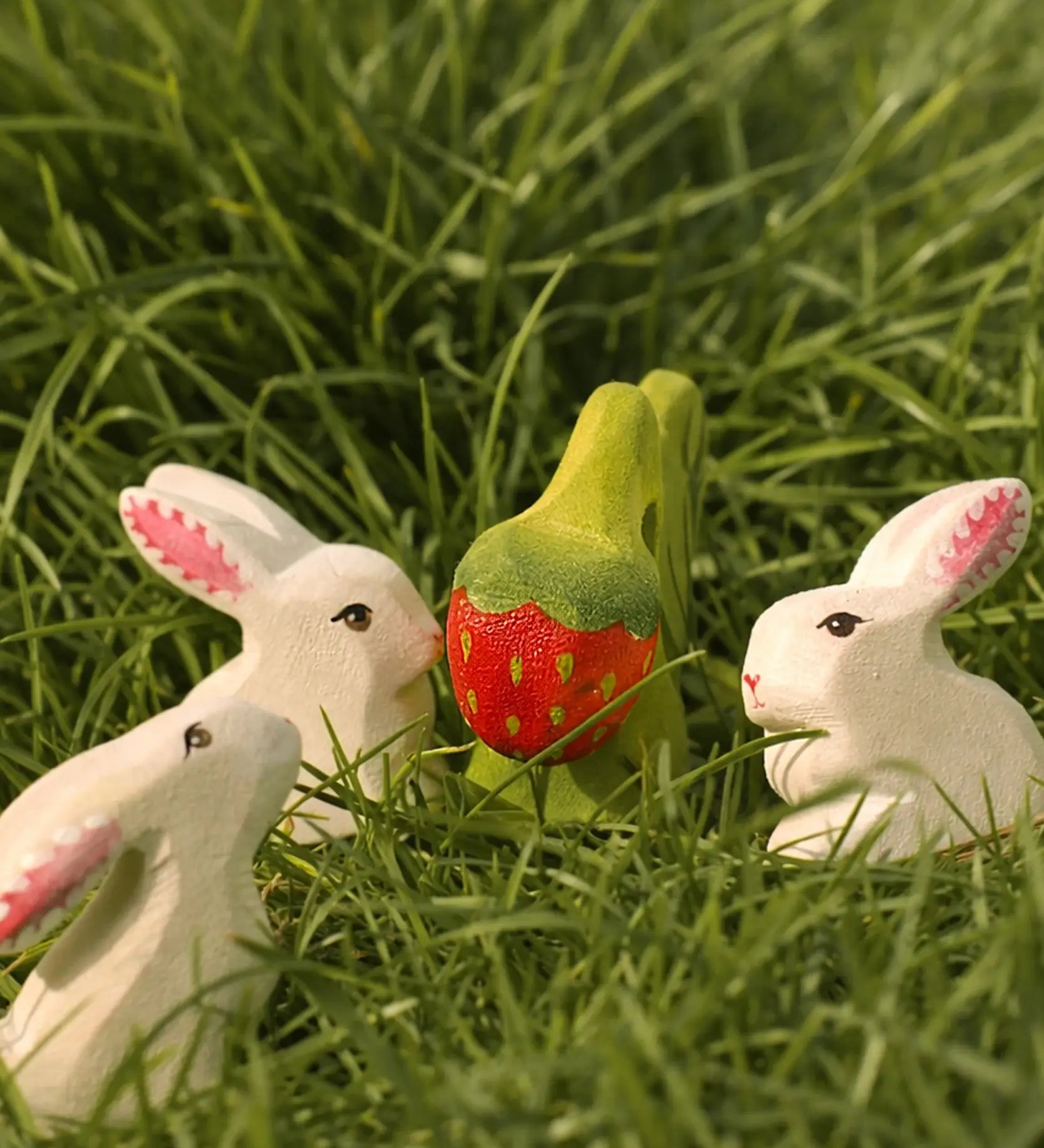 Bumbu handcrafted wooden strawberry plant on grass with white rabbits standing near