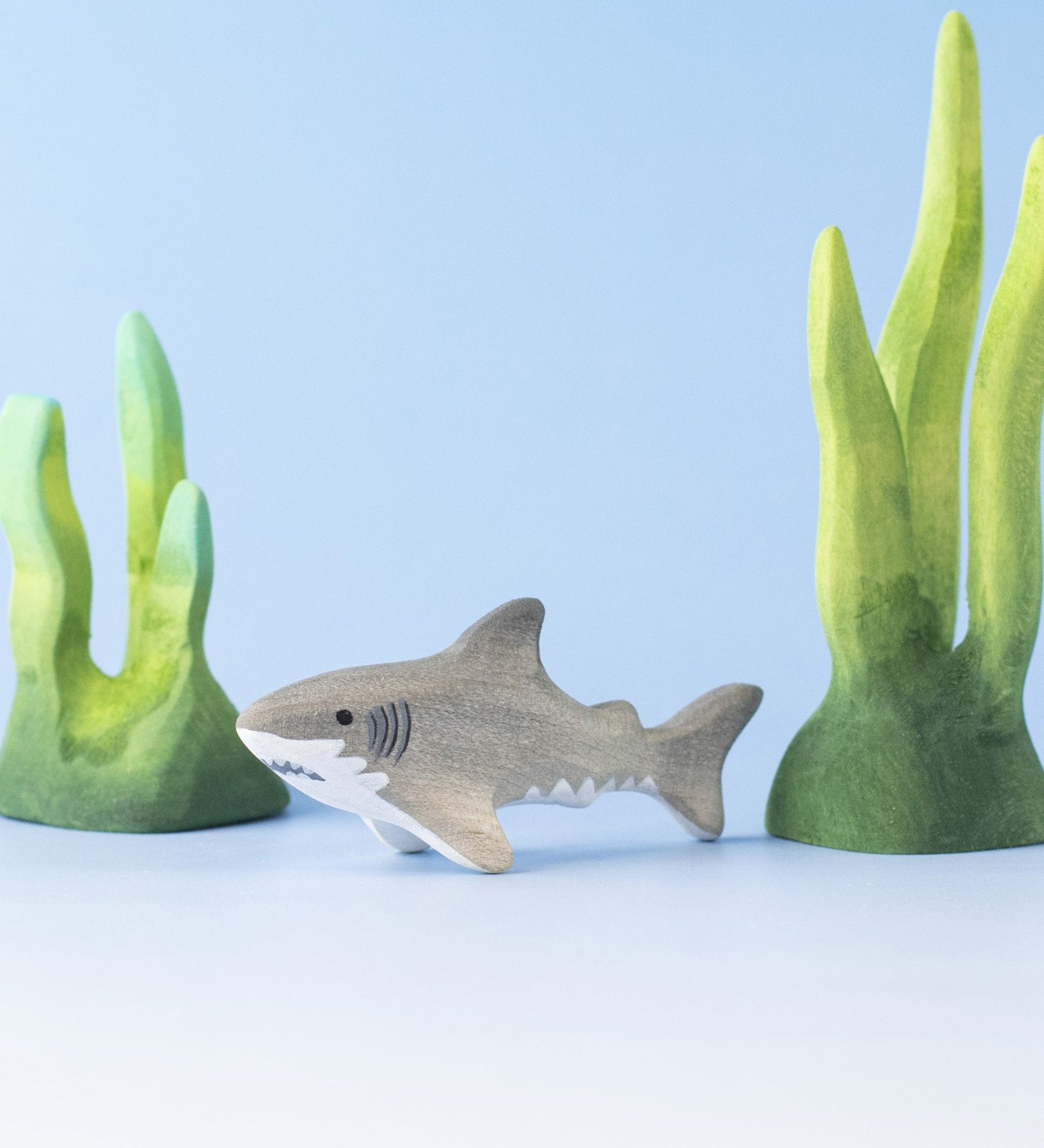 Bumbu handmade and hand painted wooden grey baby shark figure surrounded by the Bumbu green coral figures