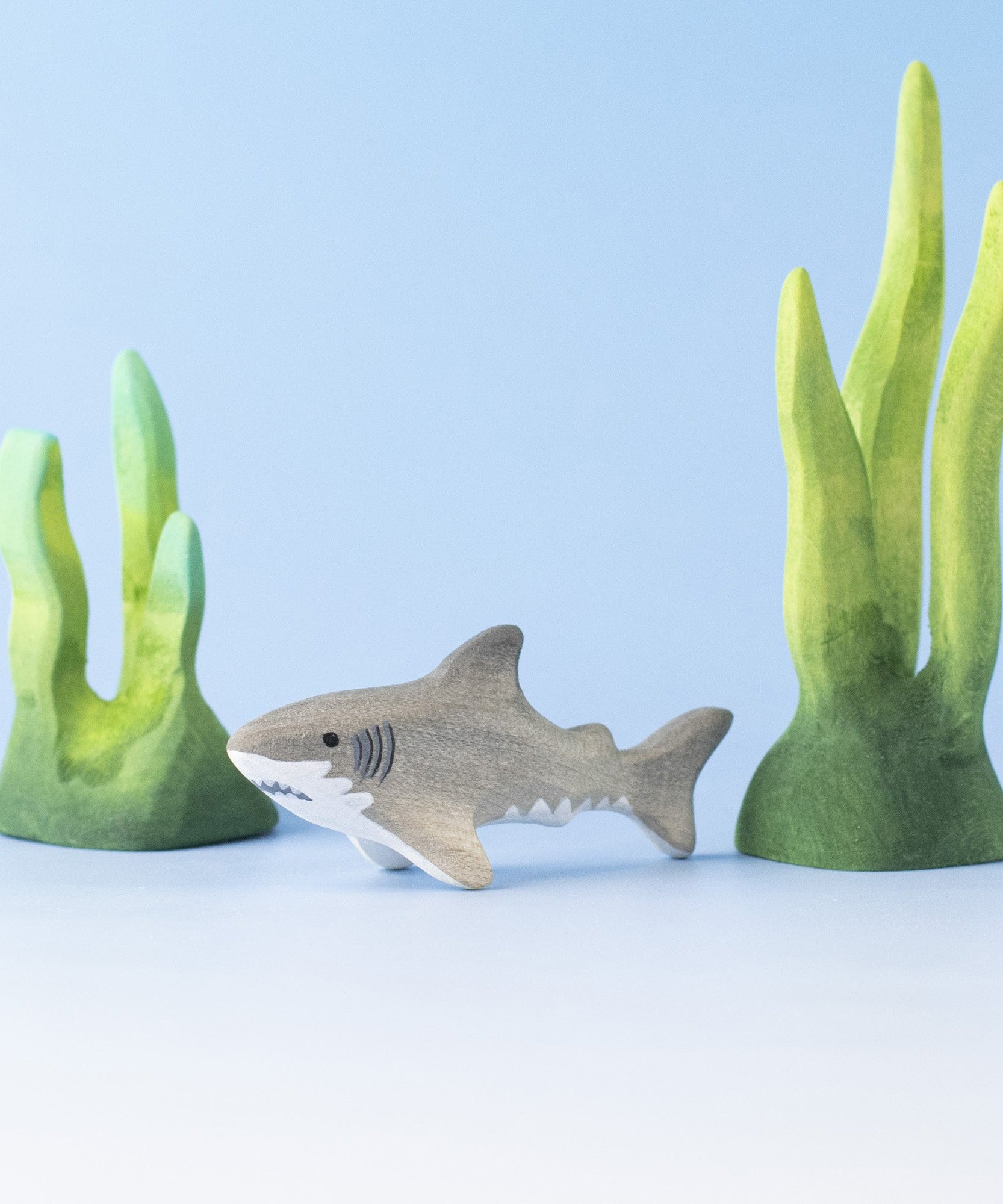 Bumbu handmade and hand painted wooden grey baby shark figure surrounded by the Bumbu green coral figures