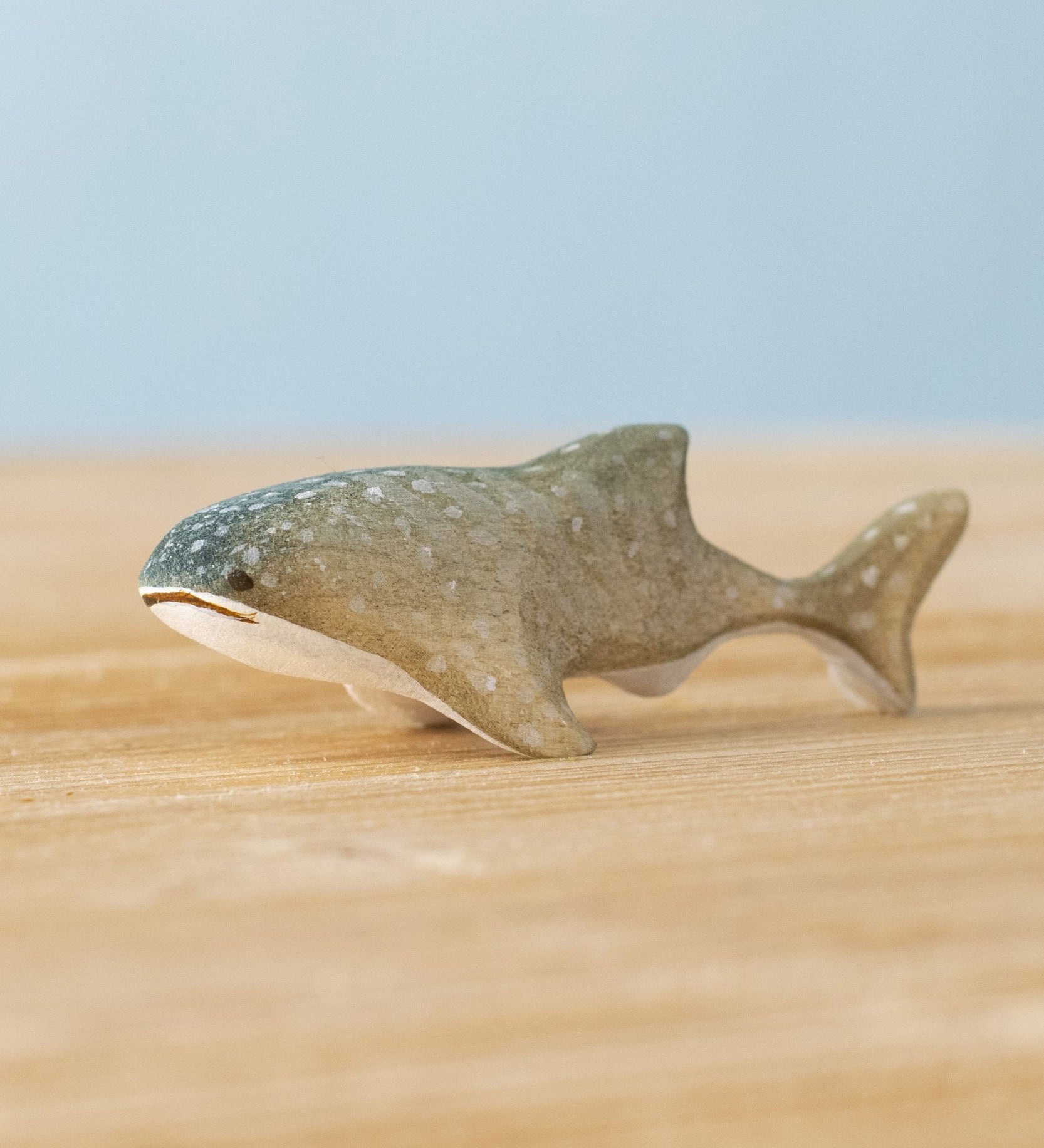 Bumbu handmade and hand painted wooden grey baby whale shark figure available at Babipur and resting on a wooden surface